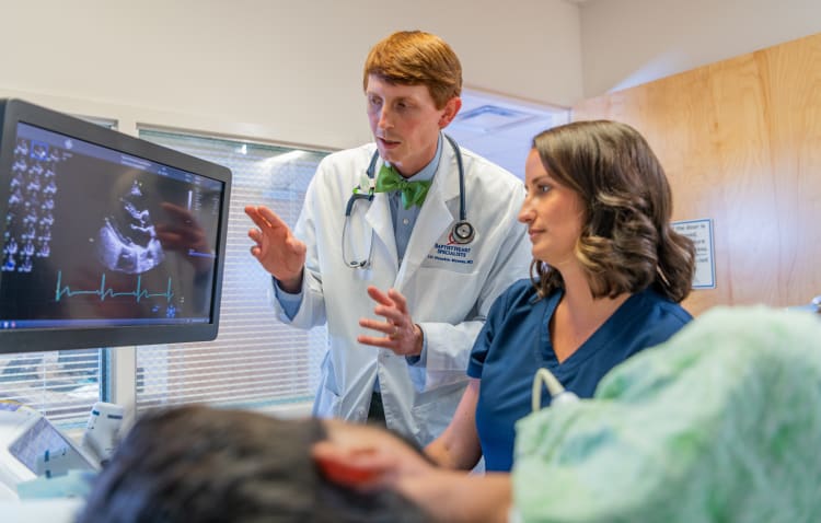 A young cardiologist looks as a screen together with an imaging specialists while scanning a patient.